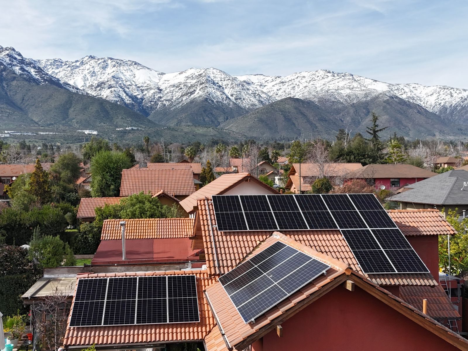 Paneles solares sobre techo de teja, con la cordillera nevada al fondo